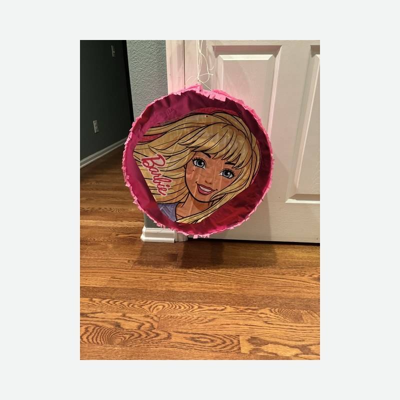 A round pink piñata printed with a fashion doll face