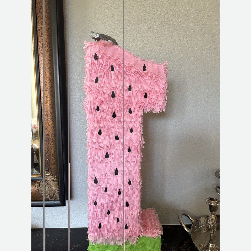 A watermelon slice piñata in pink with black seeds and a green rind